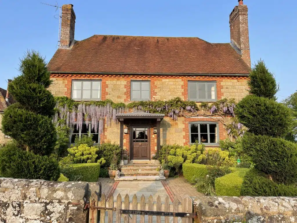 a house with bushes in front of a brick building with Jane Austen's House Museum in the background